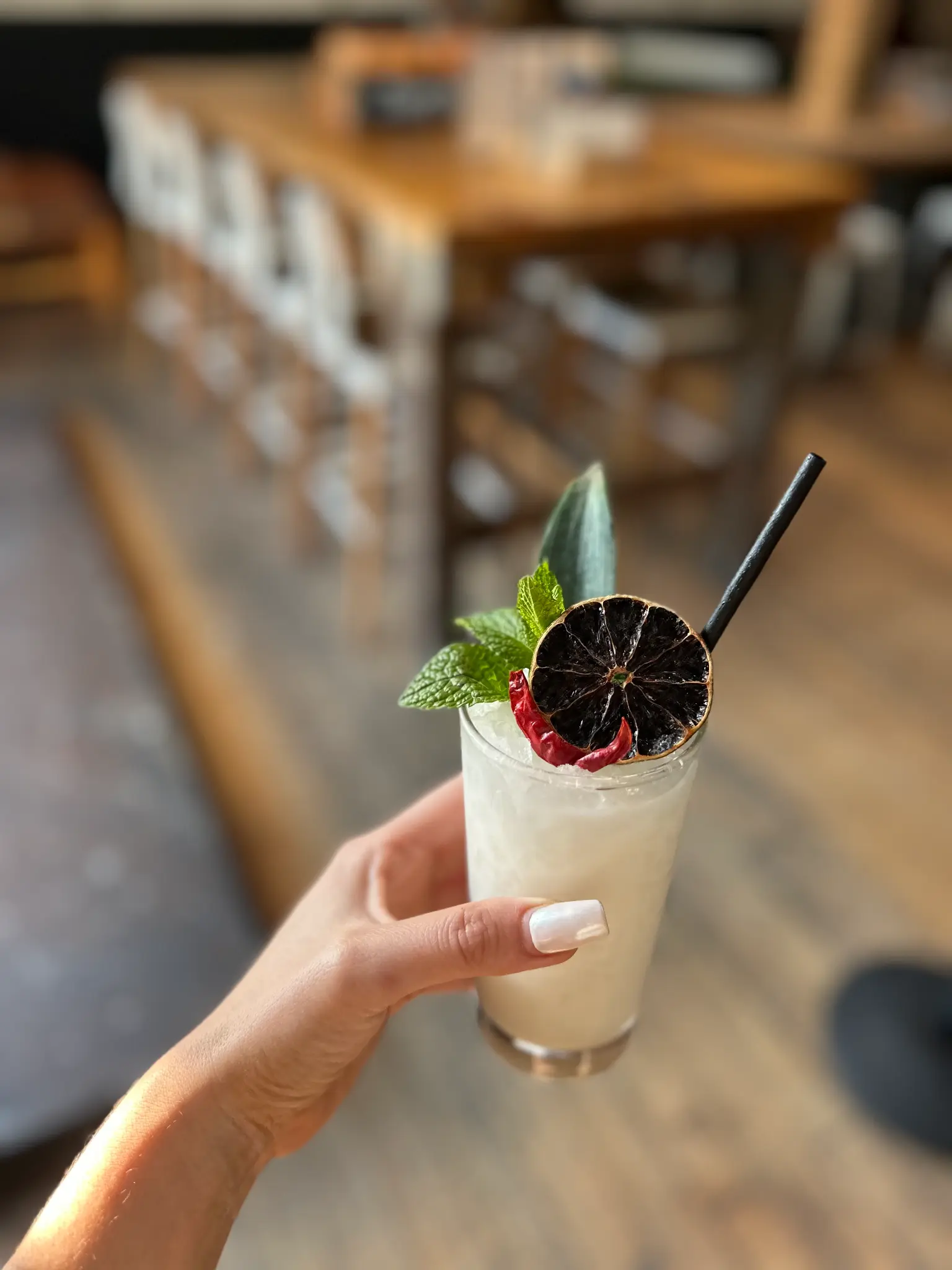 Hand holding a beautifully garnished craft cocktail with a dried citrus wheel and mint sprig at Unbearable Skee Lodge