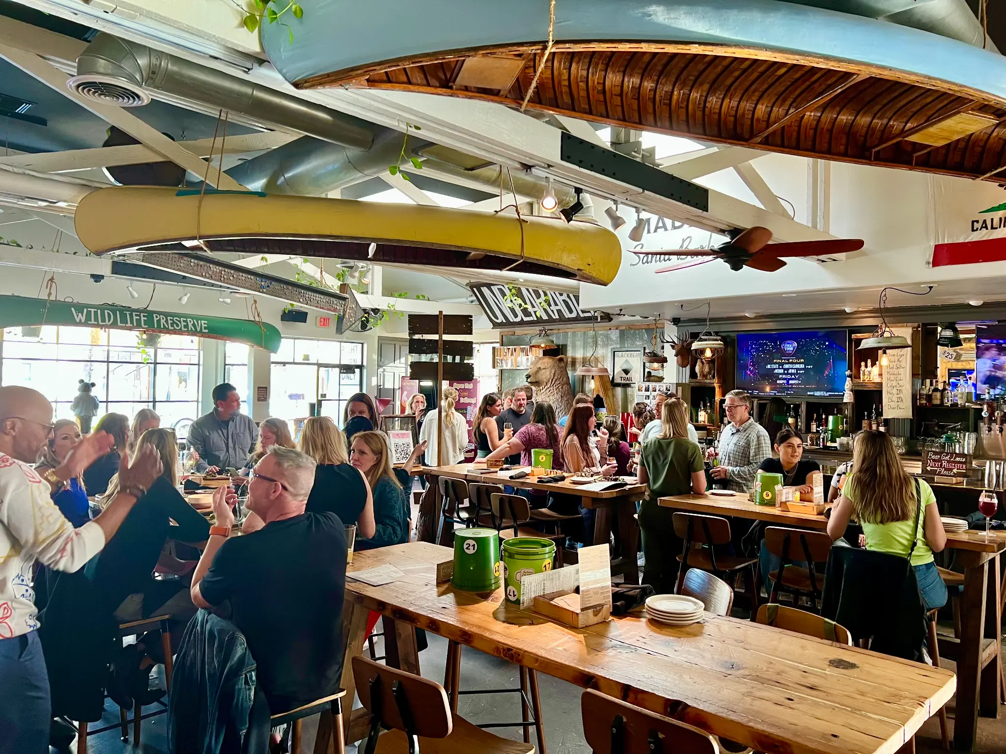 Daytime happy hour at Unbearable Skee Lodge with a packed house, canoes hanging from the ceiling, and the bear statue visible in the background