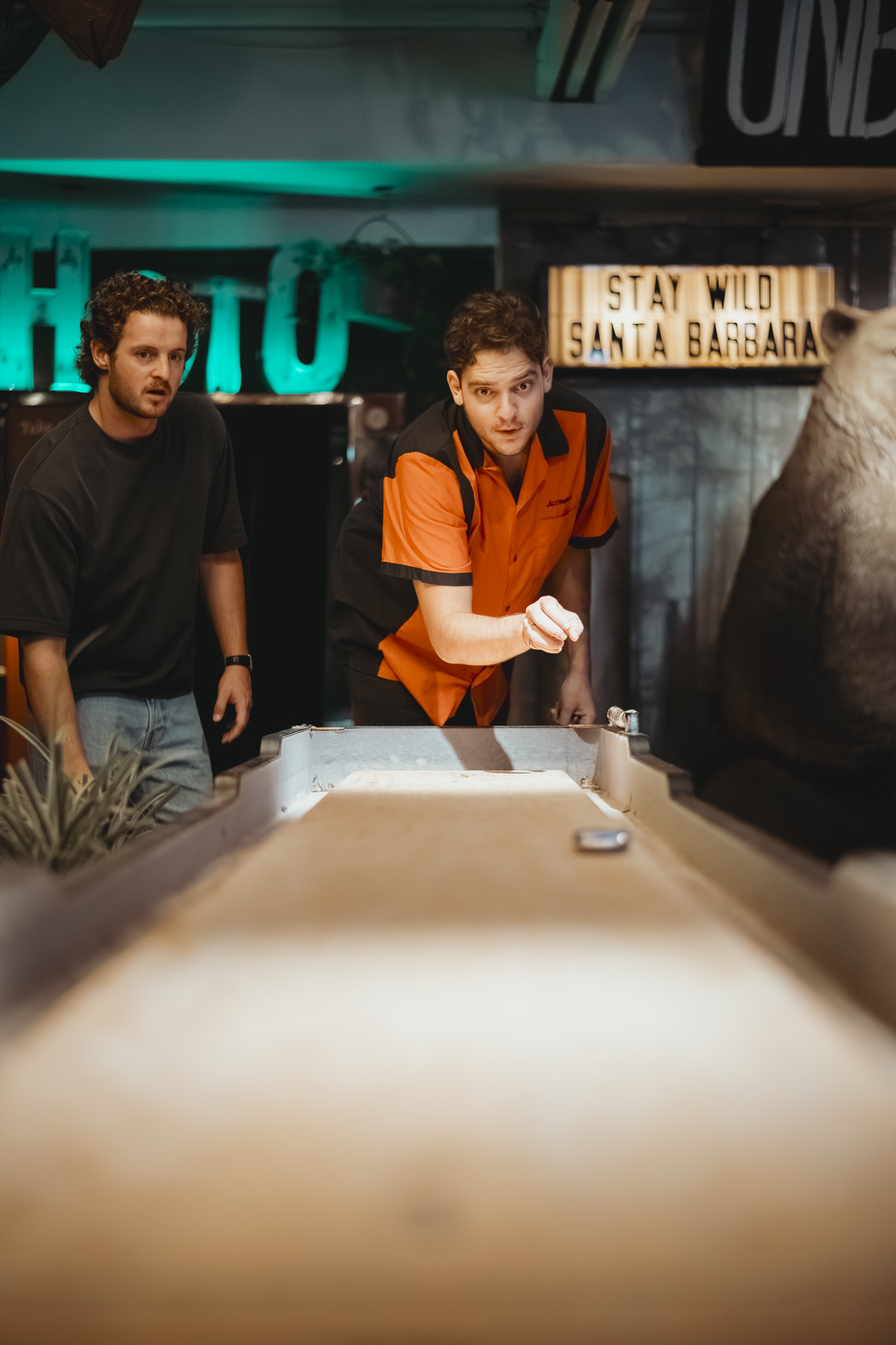 Two guests competing at shuffleboard at Unbearable Skee Lodge with the Stay Wild Santa Barbara sign in the background
