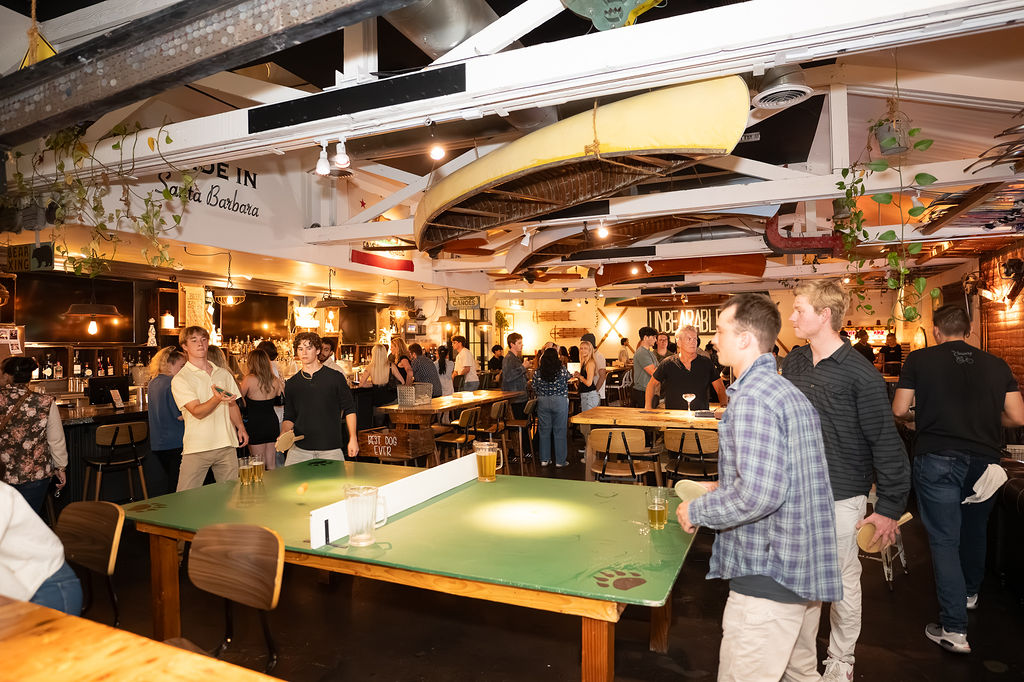 Guests playing ping pong at Unbearable Skee Lodge with a packed crowd and the UNBEARABLE sign visible in the background